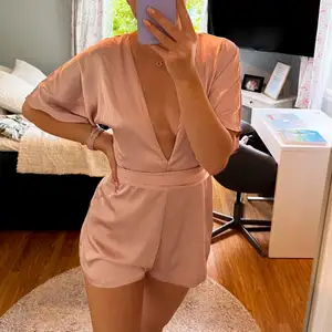 Super skön och galet fin deep v-neck silky playsuit från NA-KD. Den är i en ljus rosa färg som skimrar. Otroligt fin öppen rygg. Helt slut såld på deras hemsida. Endast använd ett fåtal gånger. Storlek 36.