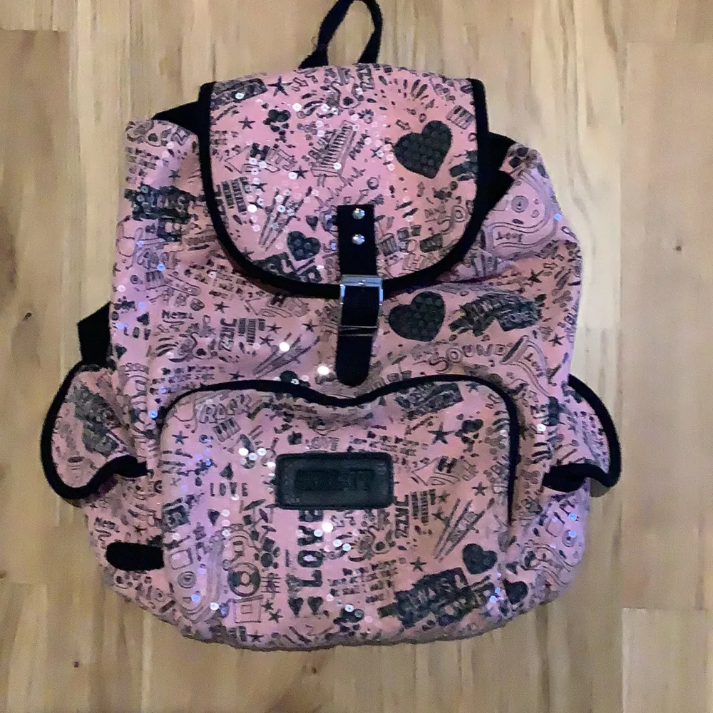 Det är en rosa väska med genomskinliga glansiga paljetter på och mönster, det finns många olika fack inuti och utanpå väskan/ryggsäcken. Den har också justeringsbara axelband.. Väskor.