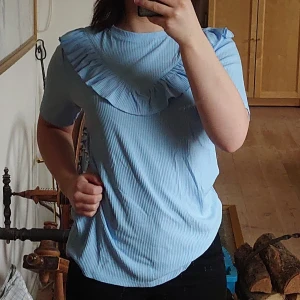 Blå t-shirt med volang - Ljusblå tröja med volang från Zoul. Är i bra skick. Pris kan diskuteras, bättre att den kommer till användning. 