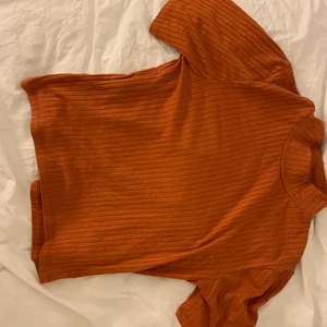 Tshirt  - Tshirt med kort hals. Något cropped i storleken. Röd-brun/orange i färgen 