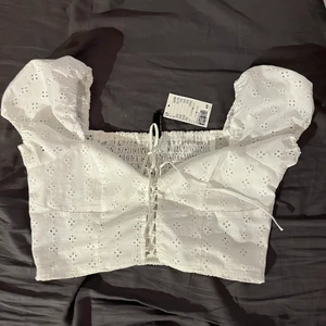 Vit topp med snörning!! - Aldrig använd, prislapp kvar. Fin vit topp med justerbara snörningar. 