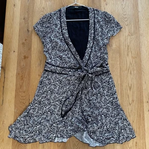 Klänning  - Mörkblå omlottklänning med vita blommor. Från Bikbok, storlek XS. Men skulle nog passa en S med, då den är lite större i storleken. Knappt använd, och är som i nyskick!  