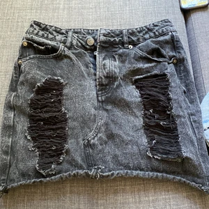 Jeanskjol med slitningar - Svart kjol från bikbok i urtvättad färg med slitningar på låren. Storlek S. Möts i Stockholm