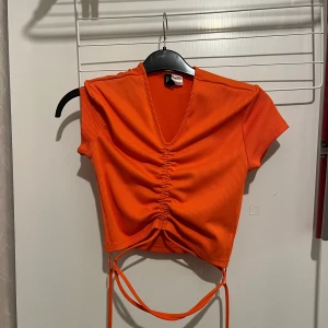 Orange kort topp från H&M - Jättefin somrig t-shirt från H&M som knyts runt magen och ryggen! Jättestark orange färg och nyskick❤️