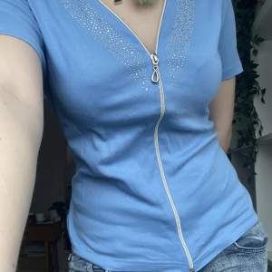 en ljusblå t-shirt från märket armani jeans som jag köpt second hand! dragkedjan är justerbar och det sitter rhinestones/strass vid kragen🥰skulle säga att den passar en storlek M också då den är liten i storleken🫶(jag vet inte om den är äkta!!)