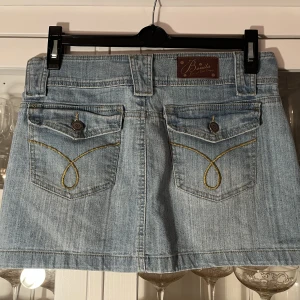 Jeanskjol - Klassisk denimblå jeanskjol i 90-tals anda! Lågmidja och kortkort. Använd men bra skick, passar strl 9/10 passar strl 34/36. 