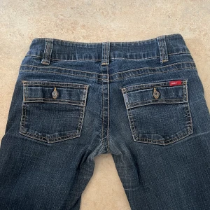 Jeans  - Så snygga lågmidjade, utsvängda jeans med coola detaljer på bakfickorna. Midja rakt över: 39cm Innerbenslängd:80cm  De är lite slitna längst ner men det är inget större man tänker på. Skriv prisförslag privat❤️