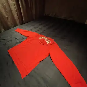 En röd supreme hoodie med SUPREME textat med paljetter på luvan, stadigt material i gott skick.