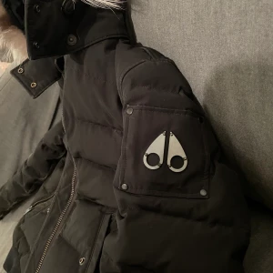 Moose Knuckles vinterjacka - En kort svart Moose Knuckles vinterjacka, passar båda tjejer och killar, specialbeställd päls, äkta! Pälsen är på vita, gråa och svarta strån. Jackan är ca 2år nästan aldrig använd då det inte riktigt är min stil. Köpt för 12.000kr. Skriv för fler bilder.