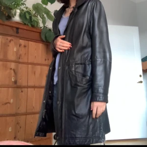 Äkta läderkappa  - Läderjacka med luva som går att ta av och på. Dragkedja och knappar och en ”slit” på sidan som även fungerar med dragkedja. Har även innerficka. Midja går att dra åt på insidan av jackan. Inga defekter men lätt sliten där bak. Frakt tillkommer!:)💗
