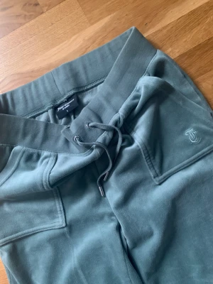 Juicy Couture byxor stl S, nyskick - Byxor i velour från Juicy Couture Bred resårkant i midjan med dragsko Fickor på vardera sida Bakfickor med lock och tryckknappar Rak modell Broderad logga framtill