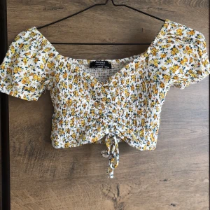 Blommig topp - Söt blommig croppad topp. Snören i mitten som man kan dra ihop tröjan med så mycket man vill