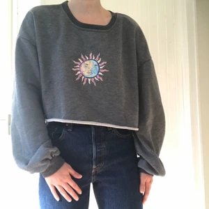 Overzised grå tröja med print - En mörk grå sweatshirt som är croppad och overzised. Den har ett sol/måne print. Tröjan är gjord av polyester och är i storlek M. Tröjan är i nyskick men använd nån gång.
