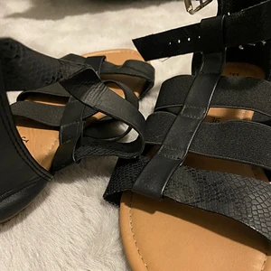 Sandaler  - Svarta sandaler som du kan spänna på sidan, inte så högklackade så det är väldigt enkelt och smidigt att gå med dem. Ormskinn aktigt på lite av tyget.  