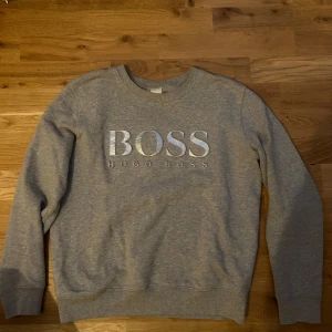 Grå sweatshirt från Hugo Boss - Säljer en stilren grå sweatshirt från Hugo Boss med deras logga i silver på bröstet. Tröjan har långa ärmar och en rund halsringning. Storlek xs.