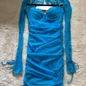 Blå klänning från Oh Polly - Snygg blå klänning från Oh Polly med långa ärmar och en tight passform. Klänningen har en rynkad design och knytband vid ärmsluten. Perfekt för en kväll ute! 💙