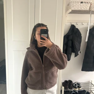 Brun teddyjacka med dragkedja - Mysig brun teddyjacka med dragkedja framtill. Perfekt för kyligare dagar med sin fluffiga och varma design. Jackan har långa ärmar och en bekväm passform som ger en avslappnad look.