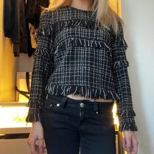 Svart och vit rutig tröja från Zara - Säljer en svart och vit rutig tröja från Zara. Tröjan har långa ärmar och fransiga detaljer som ger en unik look. Perfekt för att addera lite stil till din garderob.