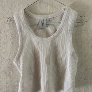 Vit ribbad linnetopp från Collusion - Säljer en stilren beige ribbad linnetopp från Collusion. Toppen är ärmlös och har en rund halsringning, perfekt för en avslappnad look. Passar bra till både jeans och kjol. Hör av dig vid intresse!