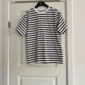 Randig t-shirt - Säljer en klassisk svartvit randig t-shirt med korta ärmar. Perfekt för en avslappnad stil. T-shirten har en rund halsringning och är gjord i ett mjukt material.