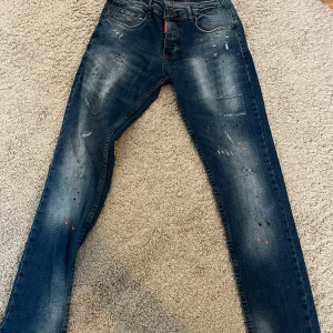 Mörkblå jeans från DSQ2 - Snygga mörkblå jeans från DSQ2 med coola slitningar och färgstänk. De har en klassisk femficksdesign och en knappgylf. Perfekta för en trendig look. Jag är runt 175 och de sitter perfekt på mig 