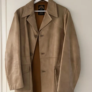 Beige skinnjacka  - Snygg beige skinnjacka från Masens i äkta getskinn. Jackan har en klassisk krage och knäppning framtill med tre knappar. Står ingen storlek, men skulle säga unisex L
