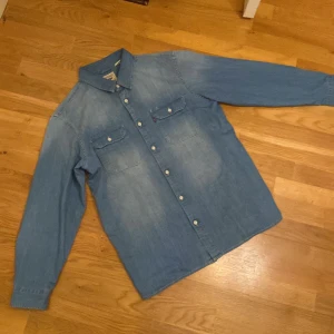 Blå jeansskjorta från Levi's - Säljer en snygg blå jeansskjorta från Levi's i modellen Jackson Worker. Skjortan har långa ärmar och knappar framtill samt på bröstfickorna. Perfekt för en avslappnad stil.