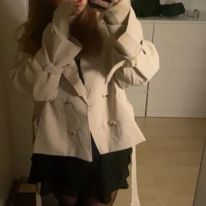  trenchcoat med knytband - Säljer en stilren beige trenchcoat med knytband i midjan och dubbelknäppning. Jackan har långa ärmar och en klassisk krage. Perfekt för att ge en elegant touch till din outfit. 💞Pris går att diskutera vid snabb affär💞Lägger ut igen pga oseriösa köpare💞