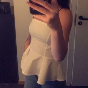 Vit axelbandslös topp - Säljer en stilren vit axelbandslös topp med volangdetaljer. Perfekt för en purrr look, kan enkelt matchas med jeans eller kjol. 