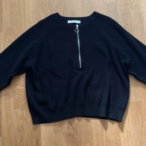 Svart tröja med dragkedja från Carin Wester - Säljer en stilren svart tröja från Carin Wester i storlek M. Tröjan har en snygg dragkedja framtill med en rund ringdetalj. Perfekt för en avslappnad look. Blir lite smalare runt handleden.