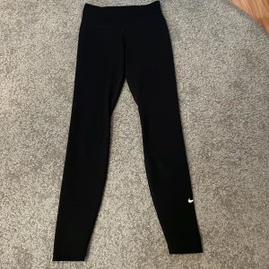 Träningstights - Snygga svarta träningstights från Nike med en liten vit logga på benet. Perfekta för träning eller en avslappnad dag. De är stretchiga och bekväma. Liten ficka bak på tightsen 