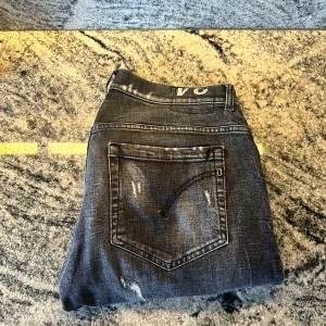 Grå jeans från Dondup - Snygga grå jeans från Dondup med slitna detaljer och en snygg tvättad look. De har en klassisk femficksdesign och knappgylf. Perfekta för en avslappnad stil. Väldigt bra skick, endast nedkortade ben, ca 90cm