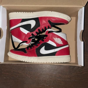 Nike Air Jordans i rött, svart och vitt - Snygga Nike Air Jordans i klassisk röd, svart och vit färgkombination. Skorna har en ikonisk design med snörning och den välkända Air Jordan-loggan på sidan. Perfekta för dig som vill ha en stilren och sportig look.