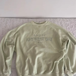 Ljusgrön sweatshirt från nelly  - Säljer en ljusgrön sweatshirt från Trend med texten 'Road to Key West Bay 1989' på framsidan. Tröjan har långa ärmar och en rund halsringning. Perfekt för en avslappnad stil.