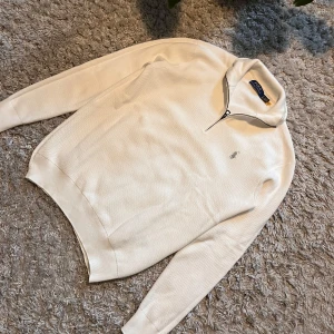 Vit tröja med dragkedja från Polo Ralph Lauren - Säljer en stilren vit stickad tröja från Polo Ralph Lauren med dragkedja och broderad logga på bröstet. Perfekt för en avslappnad och snygg look. Tröjan har långa ärmar och en klassisk passform.