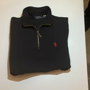 Svart tröja från Polo Ralph Lauren - Snygg svart tröja från Polo Ralph Lauren med dragkedja och röd logga på bröstet. Perfekt för en stilren look.