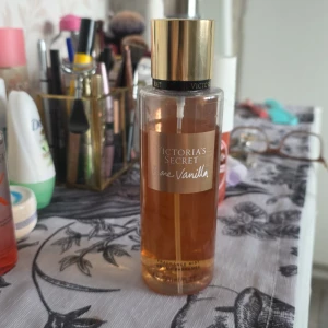 Parfym från Victoria's Secret - Säljer en parfym från Victoria's Secret med doften 'Bare Vanilla'. Flaskan är genomskinlig med en gyllene vätska och har en elegant svart och guld kork. Perfekt för dig som älskar en söt och mjuk vaniljdoft.