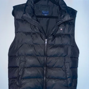 GANT Svart Väst - Svart dunväst från GANT med dragkedja framtill. Västen är välbehandlad och har inga större täcken på användning