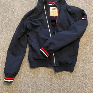 Mörkblå jacka från Tommy Hilfigher - Snygg mörkblå jacka från Tommy Hilfigher Jeans. Perfekt för en stilren look. Jackan är i mycket bra skick och passar bra nu till våren och sommaren!