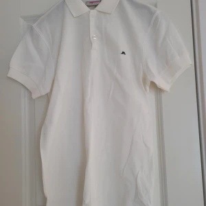 Vit pikétröja från J.Lindeberg - Säljer en stilren vit pikétröja från J.Lindeberg. Tröjan har en klassisk krage och korta ärmar med en liten logga på bröstet. Perfekt för en avslappnad men ändå snygg look. Passar bra till både jeans och chinos.