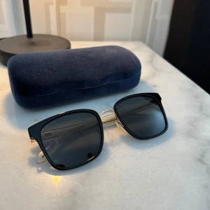 Gucci Svarta Solglasögon med Gulddetaljer - Snygga svarta solglasögon från Gucci med fyrkantiga bågar och tunna guldfärgade skalmar. Kommer med originalfodral och putsduk, samt de papper som medföljde solglasögonen. Inköpta våren 2022 men knappt använda då dem inte riktigt passade min huvudform, så mest legat och samlat damm. Finns digitalt kvitto från Zalando som jag givetvis skickar med om önskat. Vid frågor eller om fler bilder önskas så finns jag i chatten! Sista bilden är från Zalandos hemsida, inköpta för ca 3 100kr.