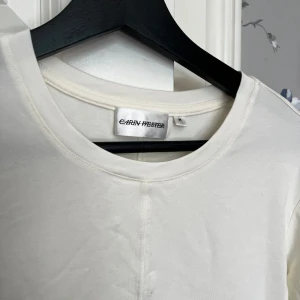 Vit långärmad tröja Carin Wester - En stilren vit långärmad tröja från Carin Wester i mjuk bomull. Tröjan har rund halsringning och en diskret söm framtill som ger en clean look. Perfekt att matcha med jeans eller kjol för en enkel och snygg outfit.