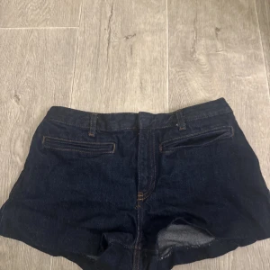 Mörkblå jeansshorts med fickor - Snygga mörkblå jeansshorts med klassiska bakfickor och bälteshällor. Perfekta för varma dagar och enkla att matcha med allt. Shortsen har en tidlös design och är gjorda i ett robust denimtyg.
