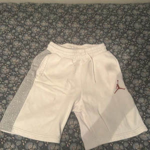 Vita Jordan shorts med grå detalj - Snygga vita Jordan shorts med grå sidopaneler som har vita prickar. Klassisk röd Jumpman-logga på ena benet och elastisk midja med snörning. Perfekta för en sportig look eller chill dagar.