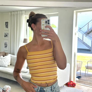 Gul randig linnetopp från New Look - Superfin gul linnetopp från New Look med tunna axelband och ribbad struktur. Toppen har röda och vita ränder och en lätt vågig kant nertill. Perfekt till jeans eller shorts för en chill sommarstil.