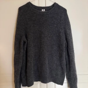 Mörkgrå stickad tröja Arket  - Mysig mörkgrå stickad tröja från Arket med rund halsringning och långa ärmar. Tröjan har en fluffig känsla och ribbade muddar vid ärmslut och nederkant. Perfekt för lager-på-lager under kyliga dagar.