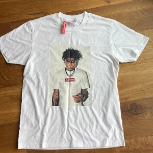 Supreme vit t-shirt med print - Passade inte därför säljer jag.Vit Supreme t-shirt i bomull med ikoniskt box logo-print på bröstet och stort foto-tryck framtill. Klassisk passform med rund hals och korta ärmar. Perfekt för dig som gillar streetwear och vill sticka ut med en fet grafisk detalj.