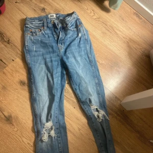 Blå slitna jeans med hål vid knäna - Snygga blå jeans med slitningar och hål vid båda knäna. Klassisk femficksmodell med ljus tvätt och raka bakfickor. Jeansen har normal passform och är tillverkade i bomull. Perfekta för en avslappnad streetstil.