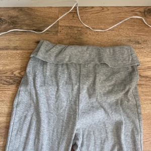 Grå bootcut mjukisbyxor - Grå mjukisbyxor med bootcut och bred, vikt midja. Byxorna är i mjukt och stretchigt material, perfekta för en chill och avslappnad stil. De har en enkel design utan synliga detaljer och är riktigt sköna att bära.