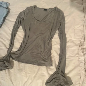 Beige militär grön topp med vid ärm - Säljer en militär grön långärmad topp från Gina Tricot med snygg, vid ärm och djup rundad urringning. Tunt och mjukt material som känns skönt mot huden, perfekt för lager på lager. Enkel att styla till både jeans och kjol.